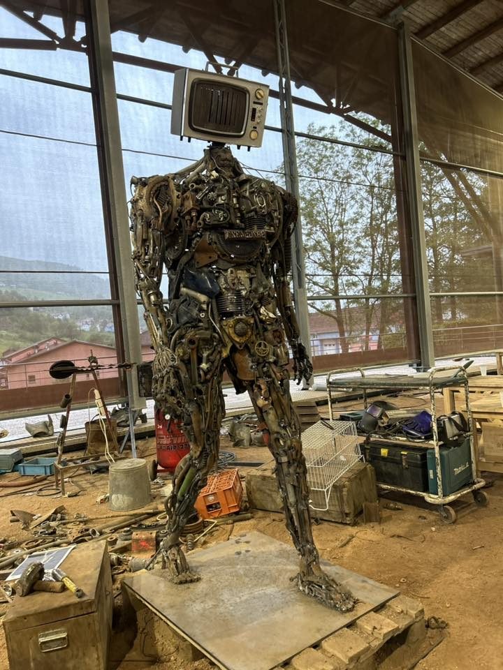 Romain Bresson — Sculpteur, né vers 1982. Fondateur de Niotte Prod, il transforme le métal recyclé en figures monumentales. Sculpture de robot en métal avec un ancien écran d'ordinateur en guise de tête.
