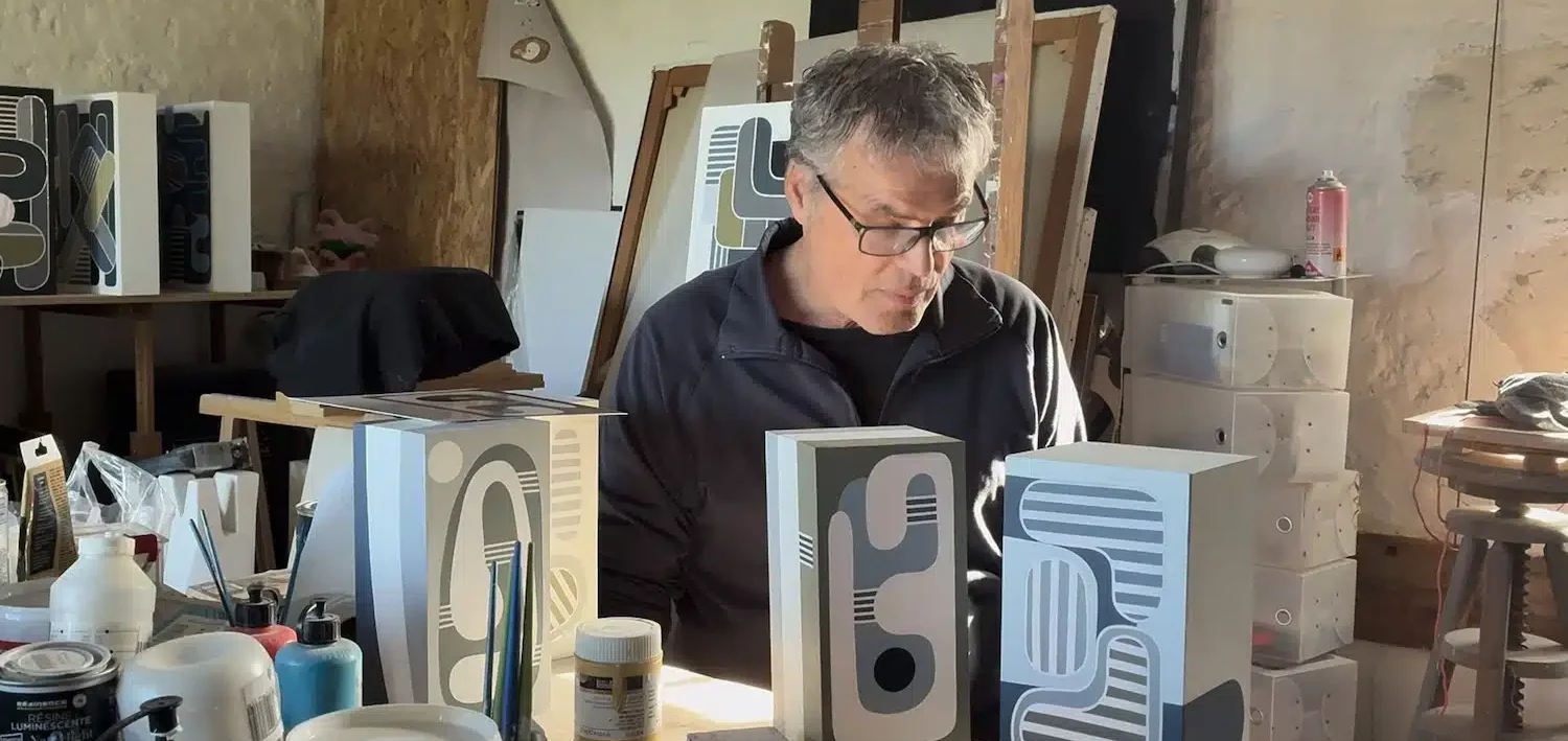 Bruno Schiepan : Artiste visuel · Peinture · Mobiles · Design · Sculptures Un homme travaille sur des objets dans un atelier, entouré de divers matériaux.